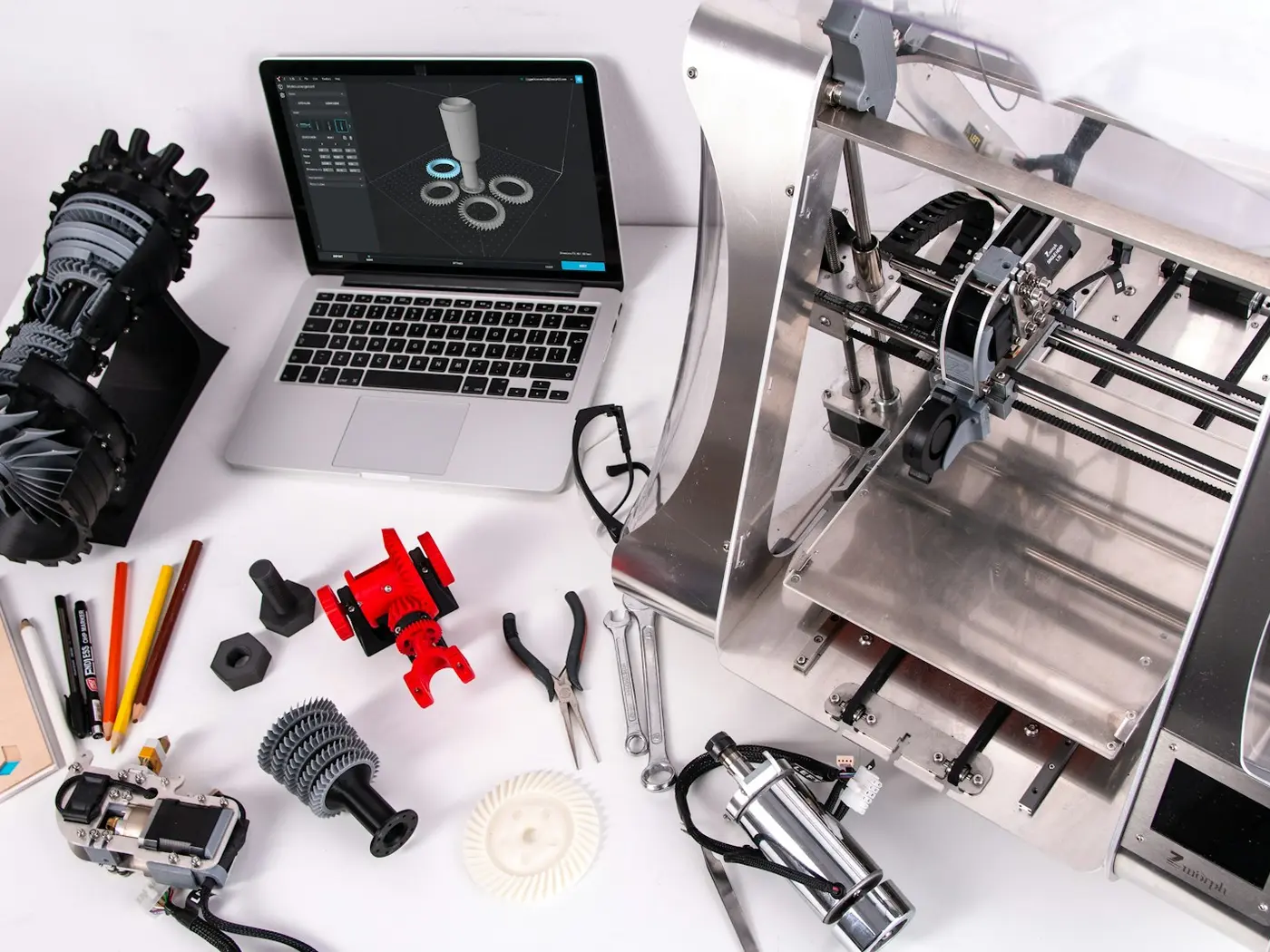 Impressora 3D ao lado de peças técnicas impressas: turbina, engrenagens e ferramentas.